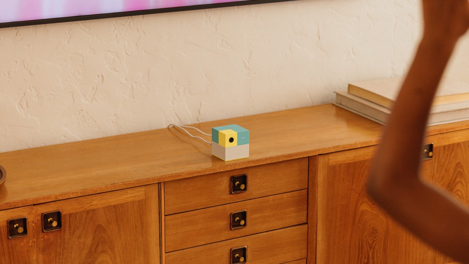 Close-up of the teal, yellow, and white Nex Playground console on a wooden cabinet, showing its front-facing camera.