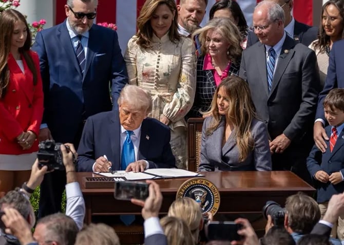 President Trump signs the Take It Down Act while seated next to First Lady Melania Trump.