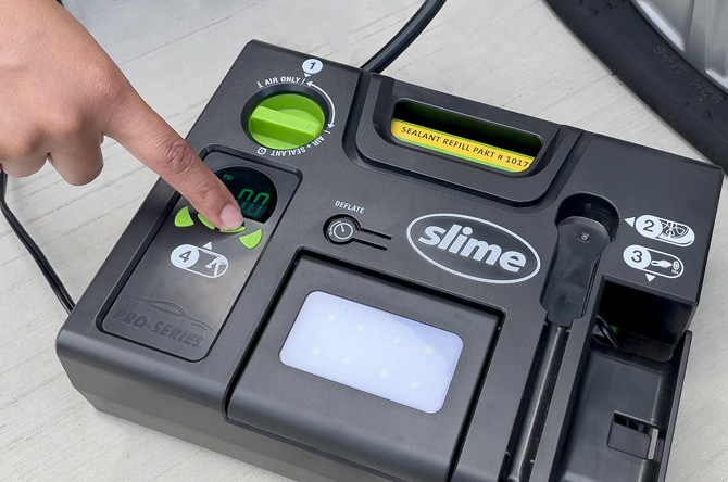 Slime Pro-Series Flat Tire Repair Kit show from the top with a hand pointing to the button used to set the tire pressure
