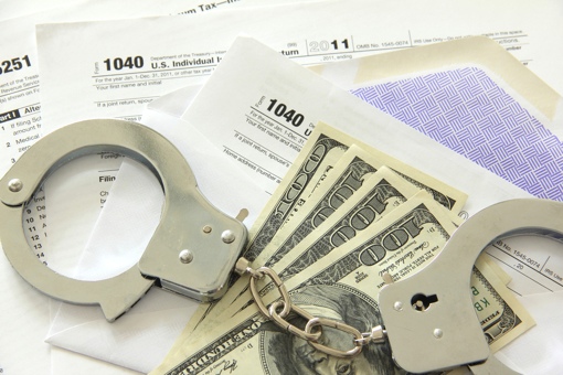 Handcuffs and cash on top of a pile of IRS forms