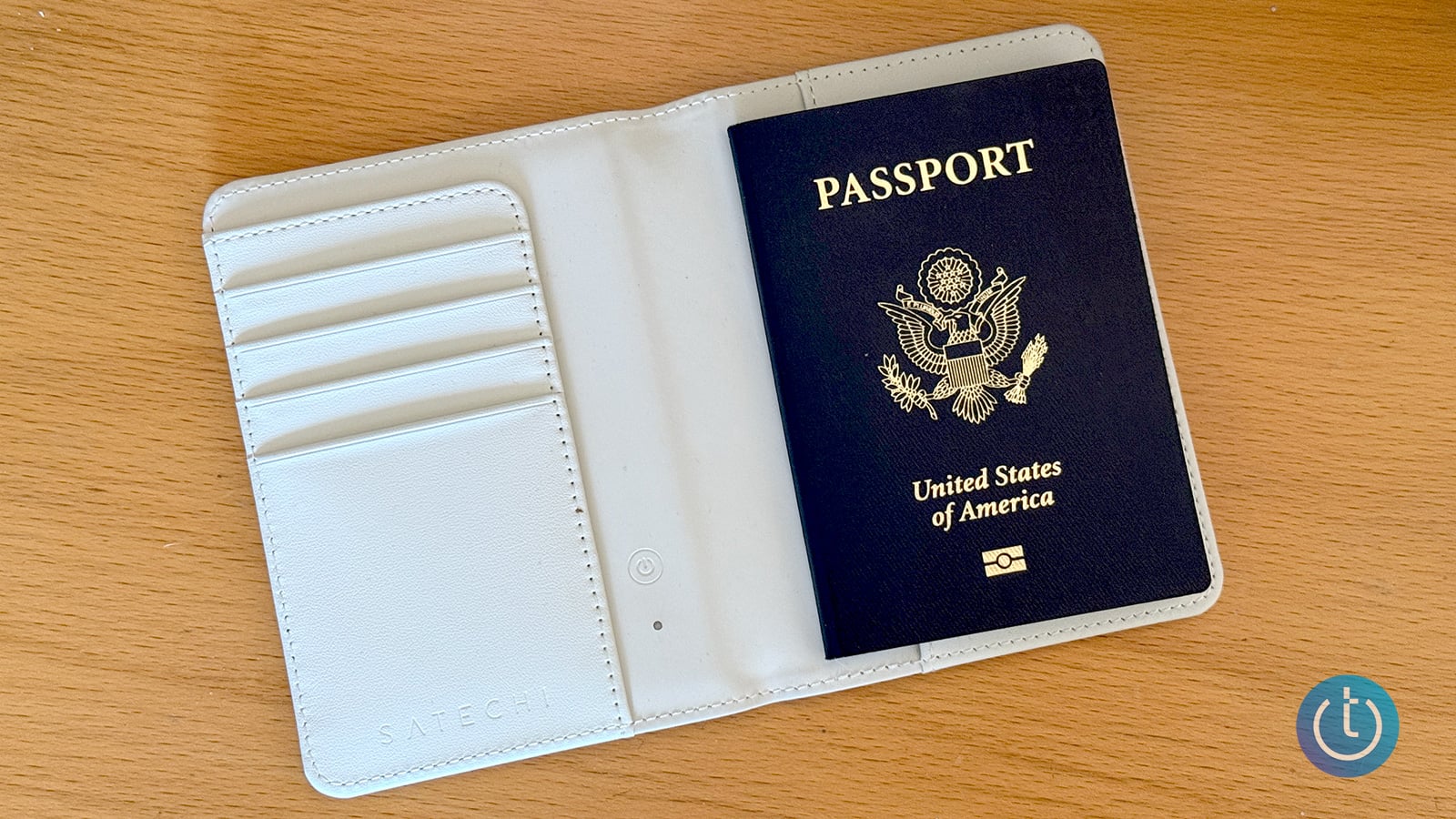 U.S. passport tucked into an open cream-colored Satechi passport holder with card slots on a wooden table.