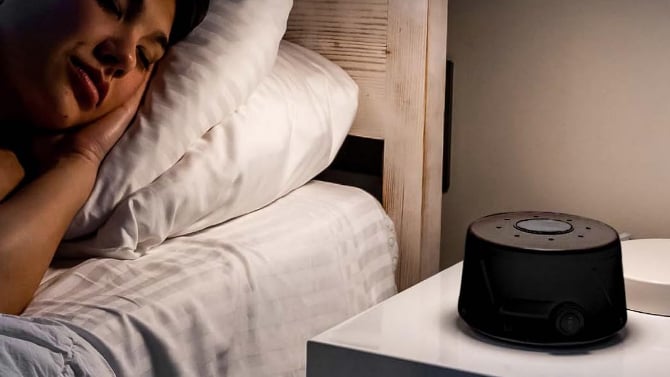 Yogasleep Dohm Classic on a nightstand next to the bed with a woman sleeping