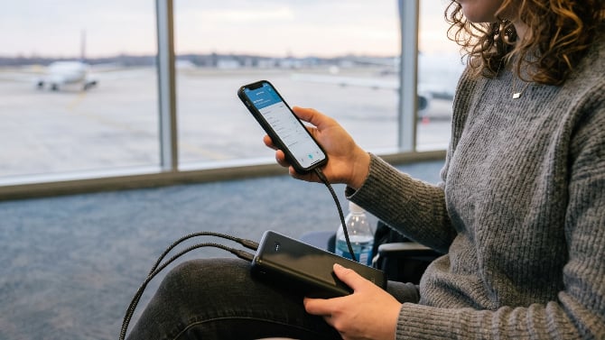 A woman holding a phone connected to a power bank at an airport