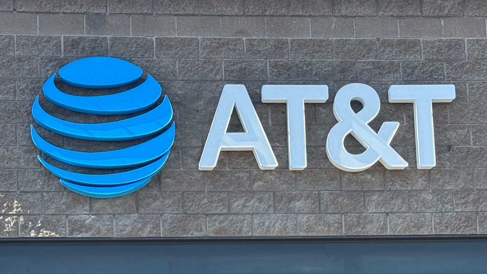 AT&T storefront sign with a blue globe logo and white lettering on a gray brick wall.