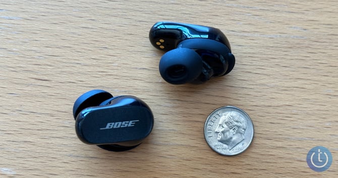 Bose QuietComfort Earbuds II on wood table with a dime. The Techlicious logo is in the lower right corner.