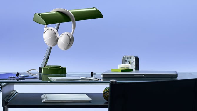 A pair of Bose QuietComfort Headphones Gen 2 rests on a desk lamp