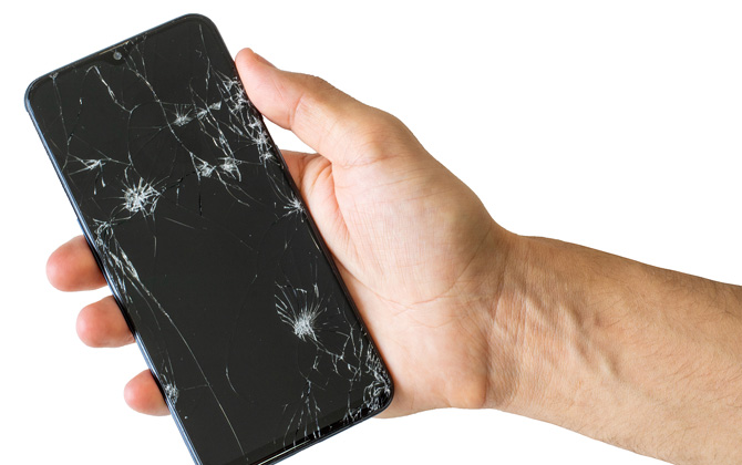 Hand holding a phone with a cracked screen on a white background.