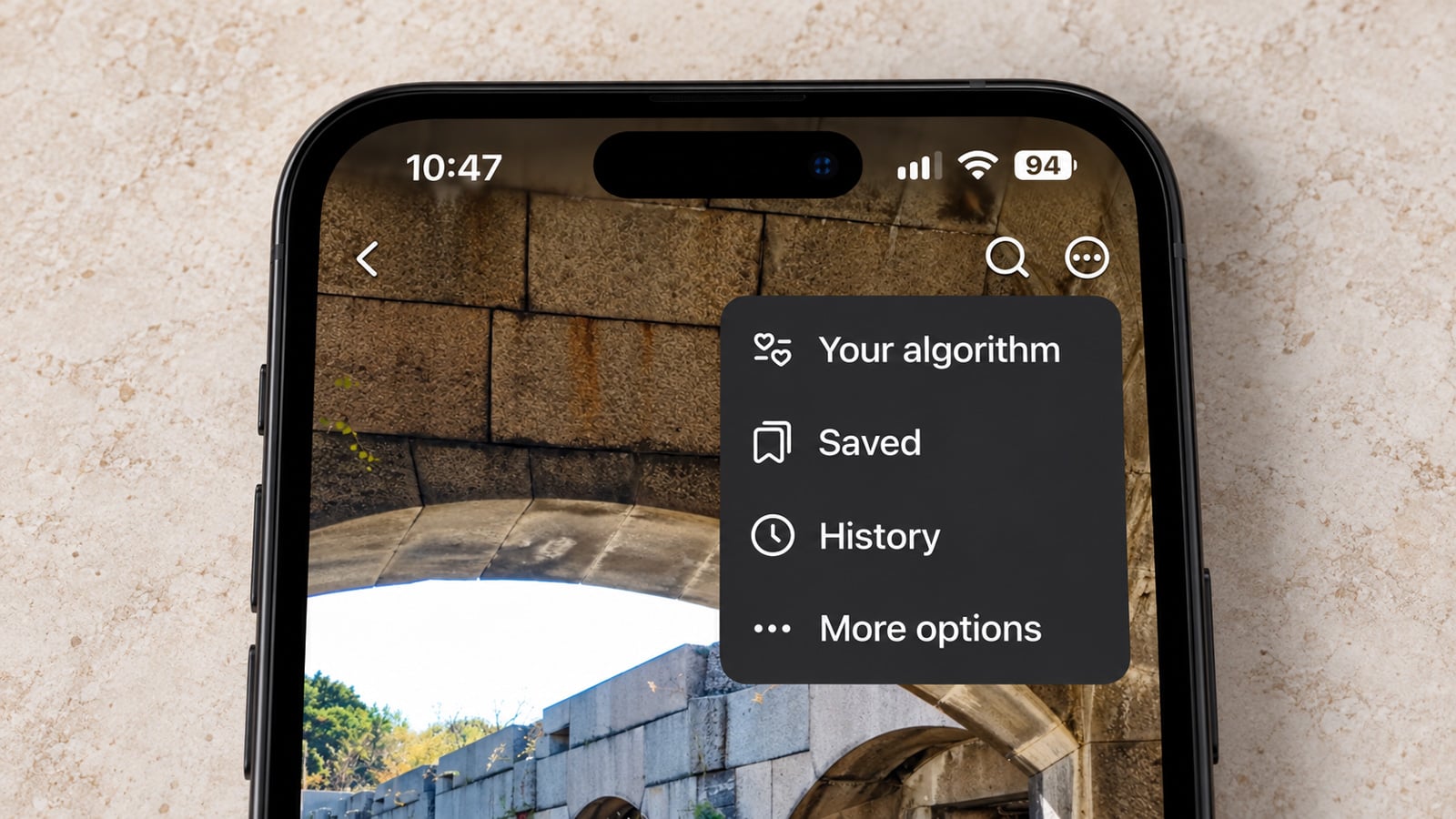 Close-up of an iPhone lying flat on a light surface, displaying a Facebook menu with 'Your algorithm,' 'Saved,' 'History,' and 'More options.'