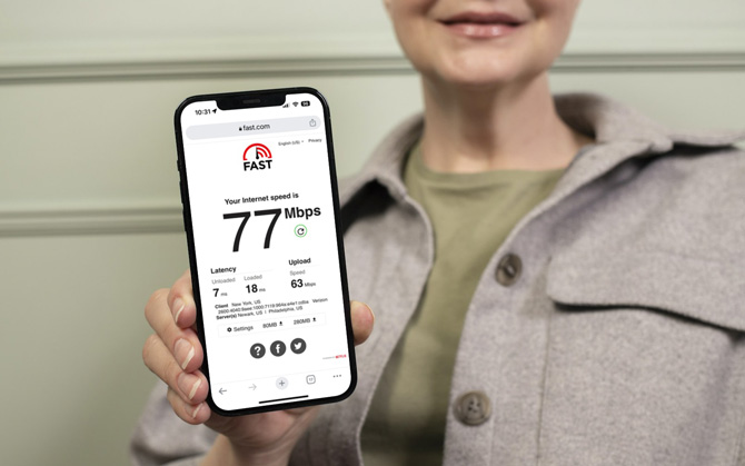 Woman holding a phone showing the results from a Fast.com internet speed check showing 77 Mbps as the download speed in 