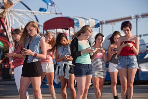 Girls at amusement park text messaging each other