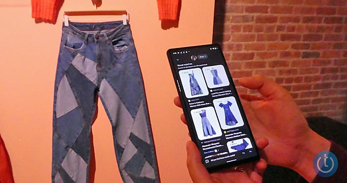 Picture of a pair of jeans hanging on a hanger against a wall with hands in the foreground holding an Android phone with a screen that shows Google search results with a dress in the same fabric.