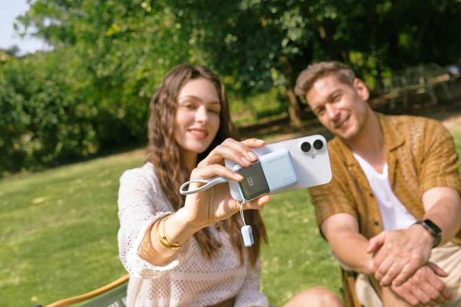 man and woman sitting in a park showing a cellphone with the INIU power bank attached to the back