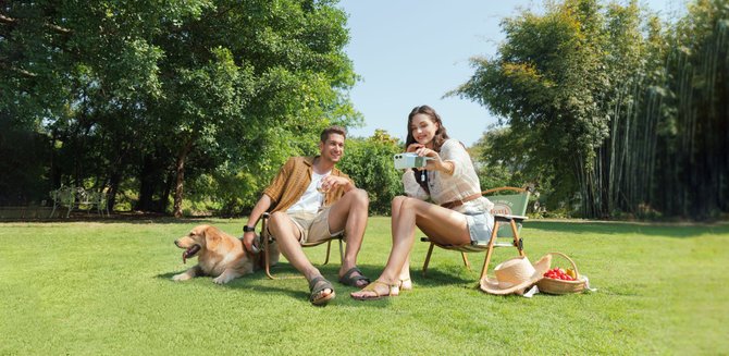 man and woman sitting on chairs in a park taking a selfie