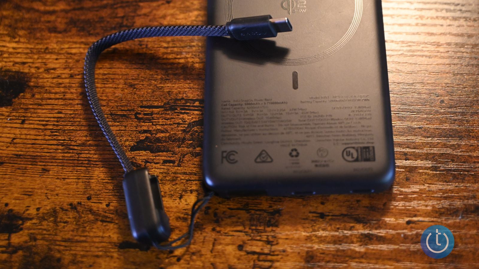 Close-up of the INIU SnapGo Air's Qi2 wireless charging circle and USB-C cable plugged into the port, with the printed capacity and certification label visible on the back of the bank.