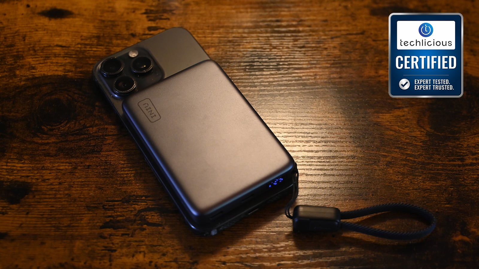 INIU SnapGo Air power bank magnetically attached to the back of a smartphone, with its braided integrated cable and cap hanging loose beside it. The Techlicious Certified seal is 