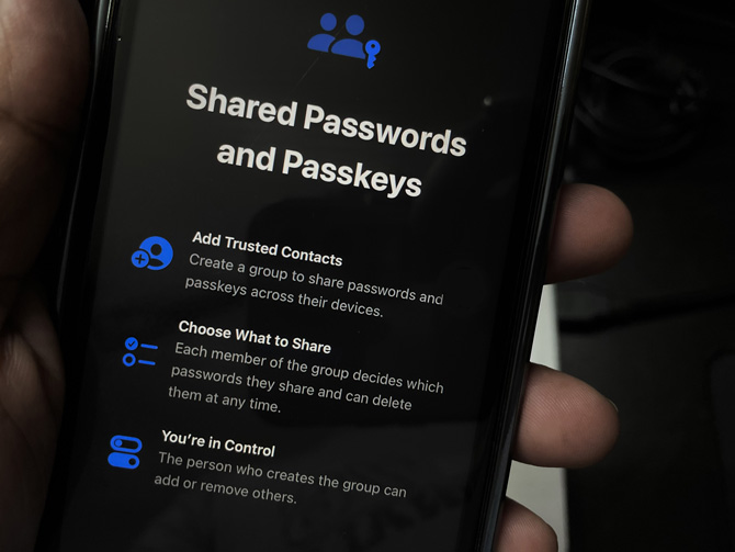 Closeup of iPhone shcreen showing the screen for sharing passwords and passkeys.  Add Trusted Contacts: Create a group to share passwords and passkeys across their devices. Choose What to Share: Each member of the group decides which passwords they share and can delete them at any time. You're in Control: The person who creates the group can add or remove others.
