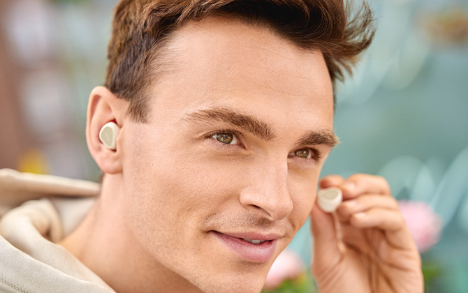 Jabra Elite 3 true wireless earbuds in beige show in one ear on male model with the other earbud in the model's hand.