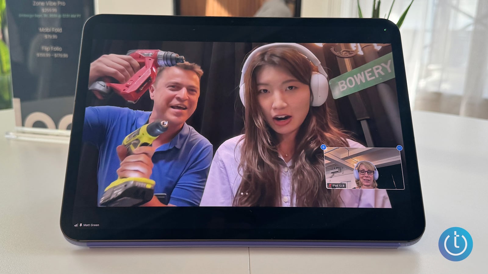 An iPad shows the writer wearing the Zone Vibe Pro on a video call with a woman. A man with two drills stands behind her.