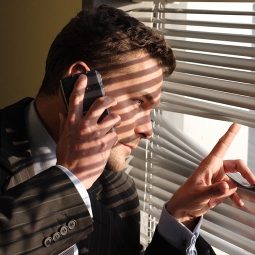 Man on phone looking through blinds