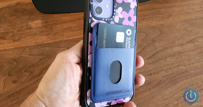 OtterBox Wallet for MagSafe in blue attached to Casetify floral pattern case. The phone is held in a hand over a wooden surface.