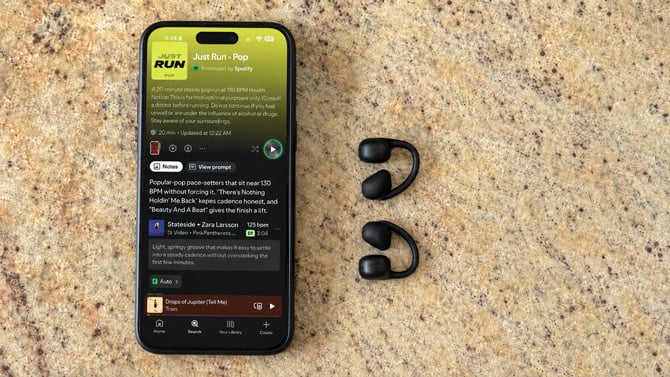 A phone shows a screenshot of the Just Run Running Mode playlist. A pair of Baseus Bowie MC2 sits on the counter to the right.