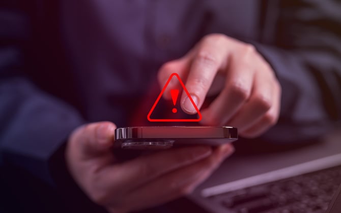 Hands holding a phone with a red caution triangle.