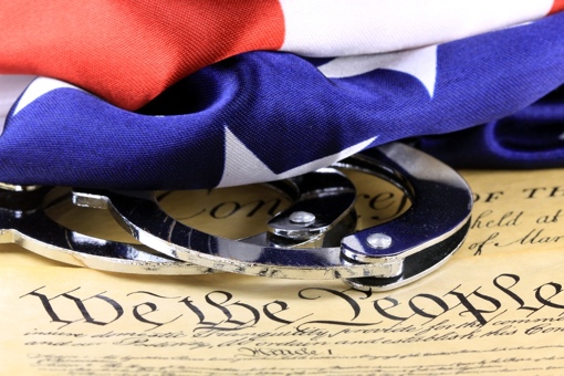 Handcuffs and American Flag on a copy of the U.S. Constitution